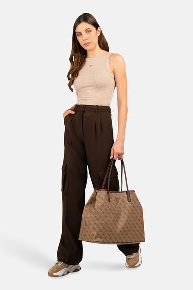Beige top zonder mouwen van Guess, gedragen met bruine broek en handtas met logoprint.
