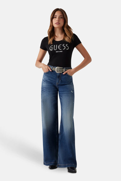 T-shirt noir à manches courtes de Guess, avec une impression blanche et porté avec des jeans larges et une ceinture.