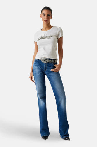 T-shirt blanc à manches courtes de Guess, avec le logo "Guess est. 1981" et porté avec des jeans et une ceinture.