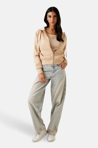 Bruine sweater met kap van Guess met open ritssluiting, gecombineerd met een tanktop en wijde jeans.