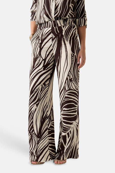 Broek in ecru met bruine print van Guess® met wijd pijpen, een abstract bladpatroon, bijpassende blouse en gouden sandalen.