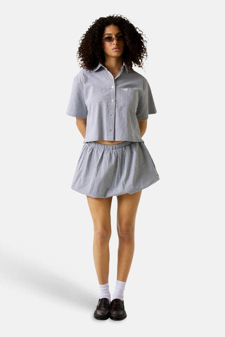 Zwart hemd met korte mouwen van Guess, met een ruitpatroon, gedragen met een rok met ruches en witte sokken.