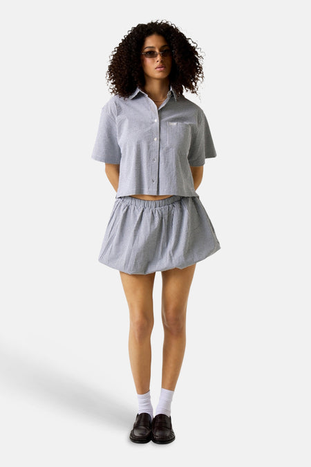 Zwart hemd met korte mouwen van Guess, met een ruitpatroon, gedragen met een rok met ruches en witte sokken.