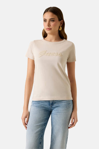 T-shirt beige à manches courtes de Guess, avec le logo de la marque sur la poitrine et porté avec un jean.