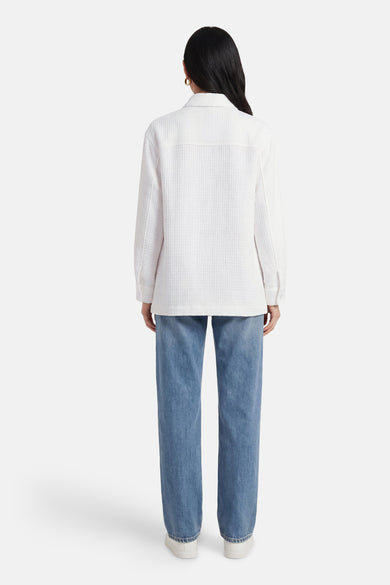 Chemise blanche Guess, dos, à manches longues, portée avec un jean bleu et des chaussures blanches.