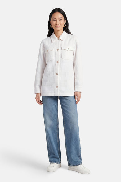 Chemise blanche Guess®, à manches longues et poches poitrine, associée à un jean bleu et des baskets blanches.
