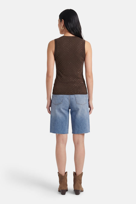 Bruine mouwloze top van Guess met zilverkleurige stippen, van achteren gezien op model met spijkershort en laarzen.