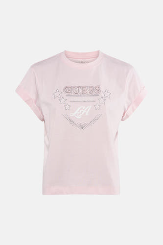 T-shirt Guess rose à manches courtes, avec logo strass et imprimé étoiles, porté avec un jean foncé et des talons hauts.