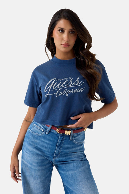Blauwe korte mouwen t-shirt van Guess met witte scriptprint, gedragen door model met jeans en rode riem, front view