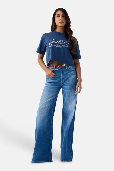 Blauwe cropped T-shirt met witte Guess California print, van Guess, gedragen met wijde jeans en rode riem, front view