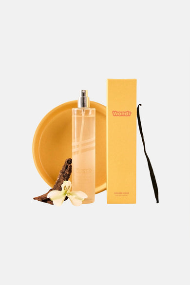 Gele parfum van WONDR CARE in heldere fles met gele doos, vanillestokje, bloem en boomschors op gele schaal.