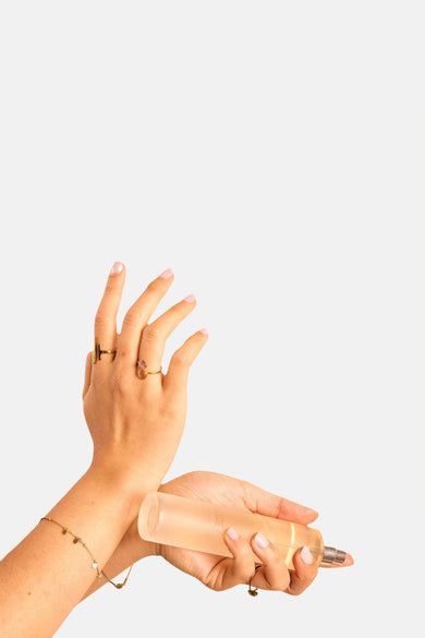 Transparant parfumflesje met lichtoranje vloeistof van WONDR CARE, vastgehouden door handen met gouden ringen en een armband.