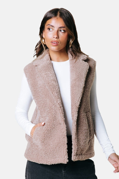 Beige bodywarmer van COLOURFUL REBEL, met zachte teddy textuur en revers, gedragen over een wit shirt.
