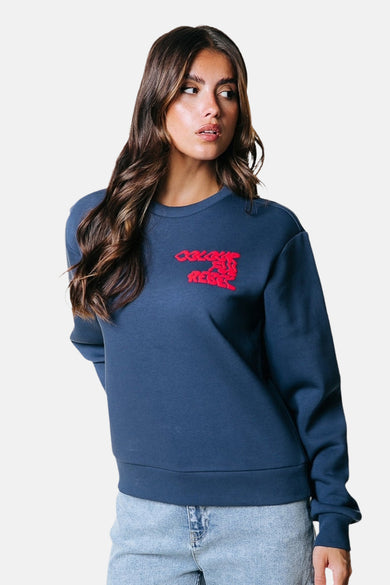 Blauwe sweater van COLOURFUL REBEL met rode print op de borst, gedragen met een spijkerbroek.