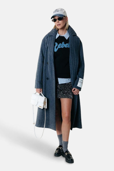 Pull-over noir à col rond de COLOURFUL REBEL, avec une impression bleue 'Rebel', superposé sur un chemisier, associé à une longue veste et des accessoires.