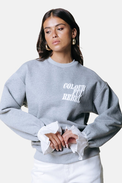 Grijze sweater van COLOURFUL REBEL met ronde hals, lange mouwen met witte ruffle-details en tekstprint op de borst.