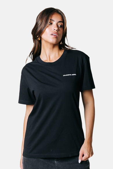 T-shirt noir à manches courtes de COLOURFUL REBEL, avec impression texte sur sur la po port porté des des boucles d'oreilles.