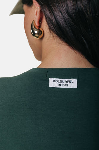 T-shirt vert à manches longues de COLOURFUL REBEL, avec une étiquette de marque dans le cou et porté avec des boucles d'oreilles dorées.