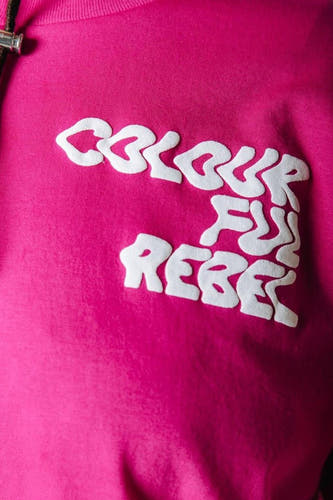 Roze T-shirt van COLOURFUL REBEL met witte, opstaande tekst 'COLOURFUL REBEL' op de borst en een deels zichtbaar zwart trekkoord.