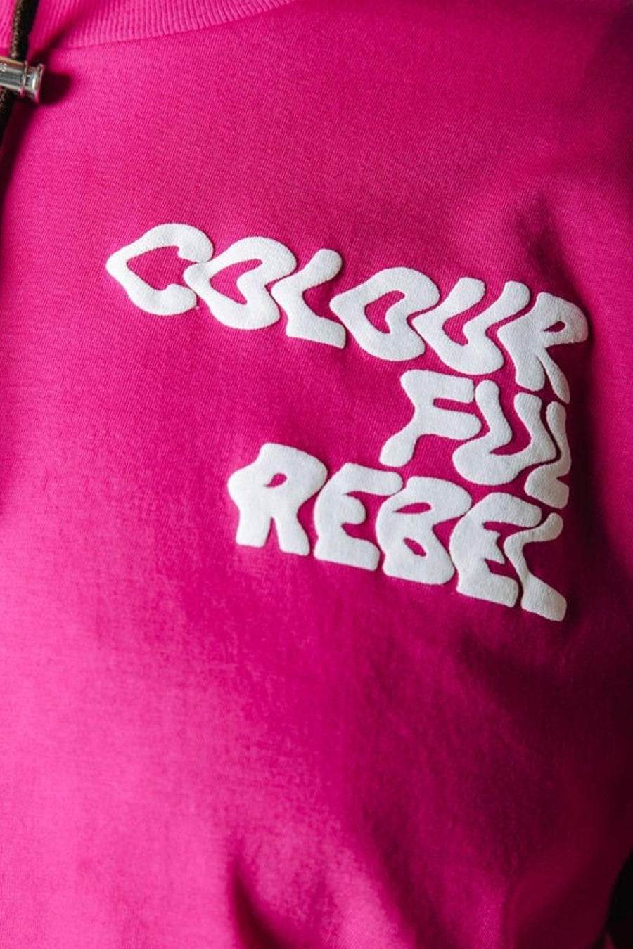 Roze T-shirt van COLOURFUL REBEL met witte, opstaande tekst 'COLOURFUL REBEL' op de borst en een deels zichtbaar zwart trekkoord.