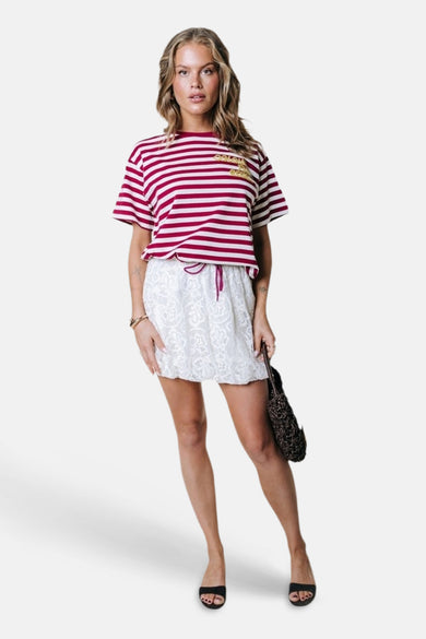 Rood-wit gestreept korte mouwen T-shirt van COLOURFUL REBEL met goudkleurig logo, gedragen met witte kanten rok en zwarte sandalen, front view.
