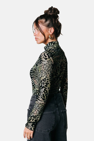 Manche à manches longues verte de COLOURFUL REBEL avec imprimés zèbre et léopard, associée à un jean noir et des boucles d'oreilles dorées.