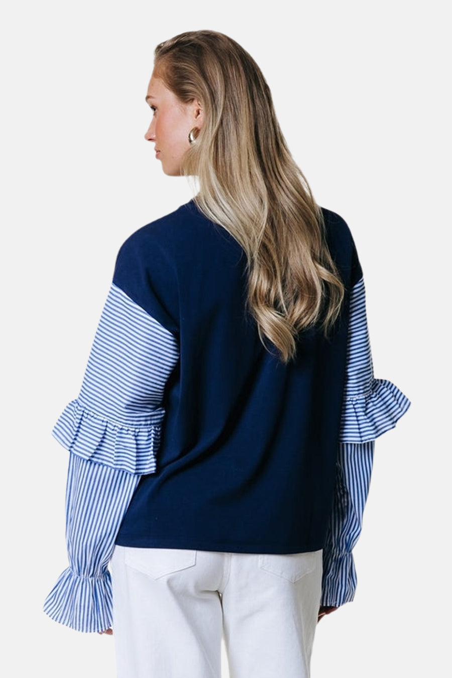 Pull bleu de COLOURFUL REBEL, avec de longues manches rayées à volants, porté avec un pantalon blanc.