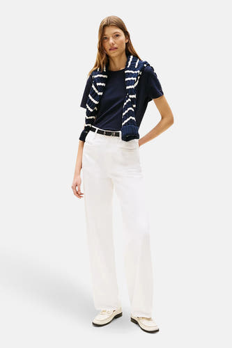 Blauw T-shirt met korte mouwen van Tommy Hilfiger, met een gestreepte trui over de schouders en witte broek.
