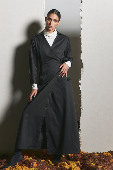 Robe noire à longues manches de YŪGEN, avec un détail plissé et une fente, portée sur une chemise blanche.