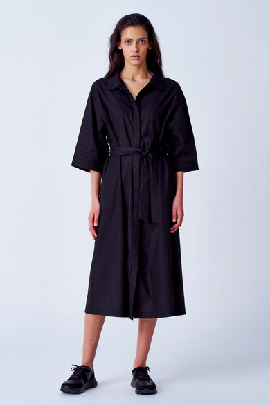 Robe noire à manches courtes de YŪGEN, avec ceinture et fermeture à glissière, portée avec des baskets noires.