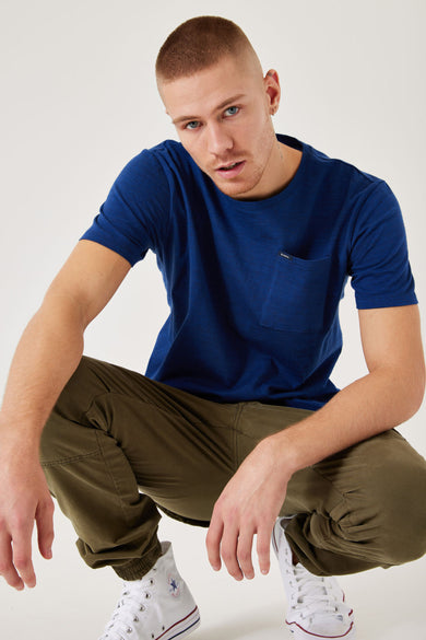 T-shirt bleu à manches courtes de GARCIA, avec poche poitrine, associé à un pantalon olive et des baskets blanches.
