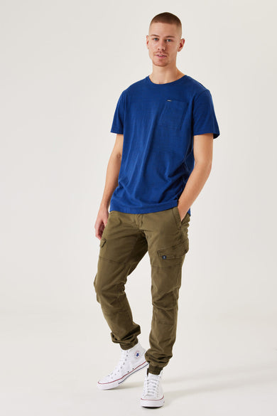 T-shirt bleu à manches courtes de GARCIA, avec une poche po poitrine et associé à des pantalons cargo verts et des baskets blanches.
