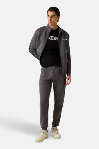 Grijs gilet van Guess, gedragen over een zwart T-shirt, gecombineerd met een bijpassende broek en crèmekleurige sneakers.