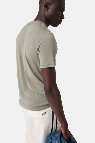 Groene korte mouwen t-shirt van Guess, zijprofiel van model met witte broek en jeansjack
