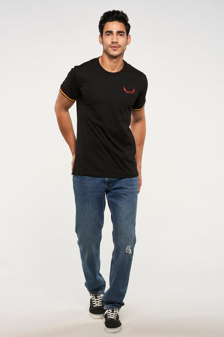 Zwart T-shirt van ZEB STYLE LAB, met korte mouwen en een rode "DEVILS" print, gecombineerd met blauwe jeans en zwarte sneakers.
