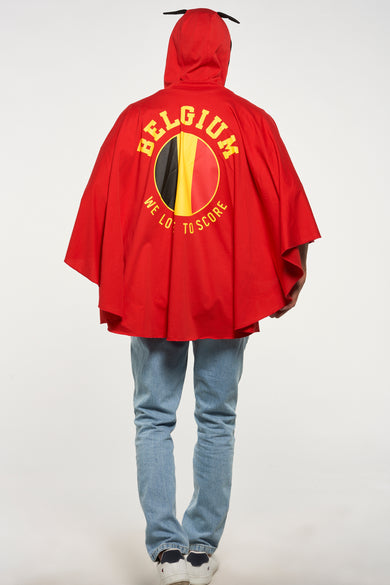 Rode poncho van ZEB STYLE LAB, met Belgische vlag en tekst op de achterkant, gedragen met een spijkerbroek en witte sneakers.
